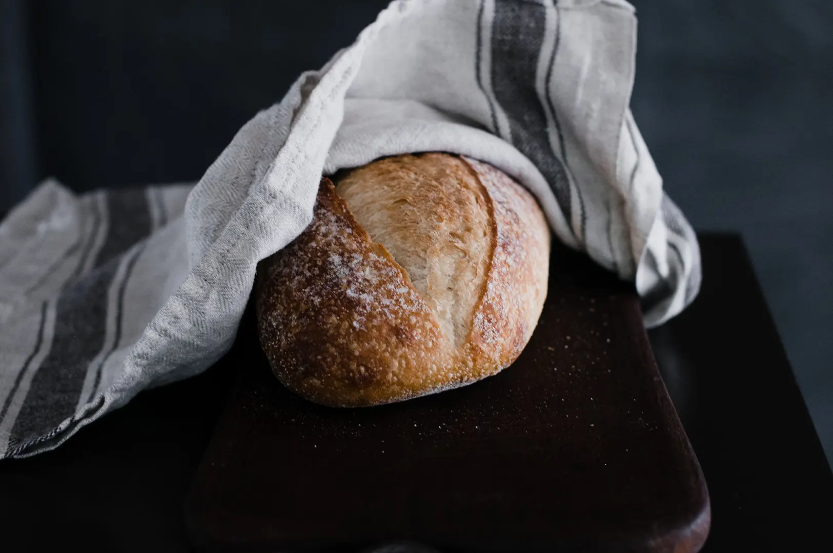 Freshly baked artisan sourdough bread on a wooden board covered with a kitchen towel.