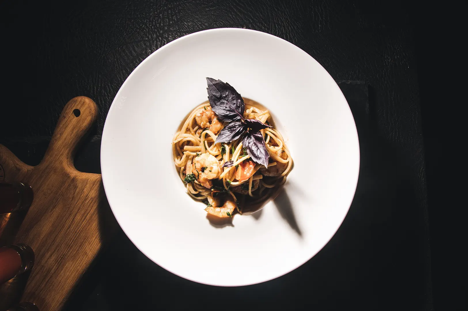 A gourmet plate of shrimp pasta garnished with a fresh purple basil leaf on a dark wooden table.