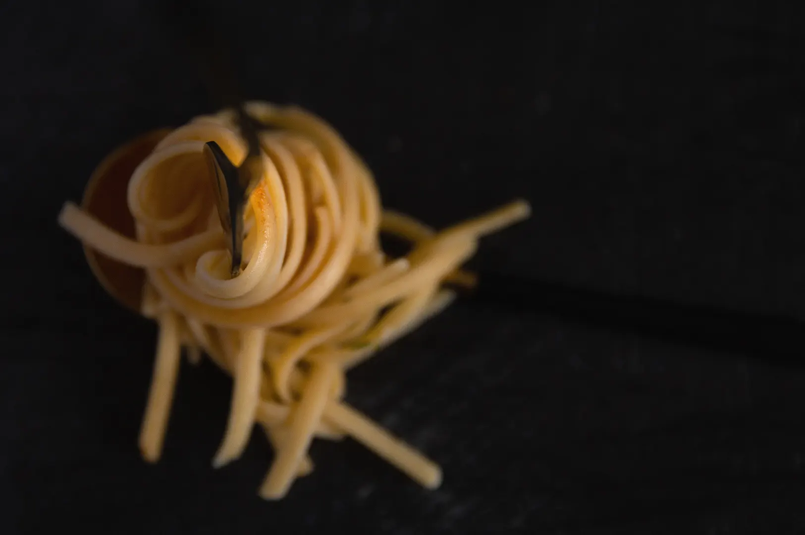 Smooth creamy silky pasta twirled on a fork against a dark background.