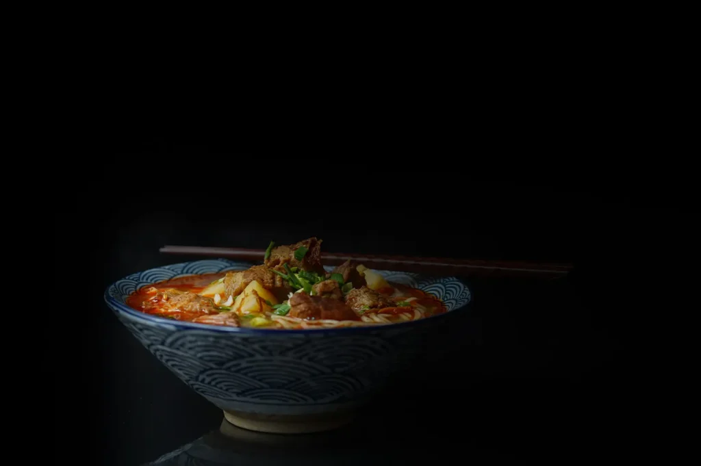 Bowl of spicy beef noodle soup with chopsticks against a black background.