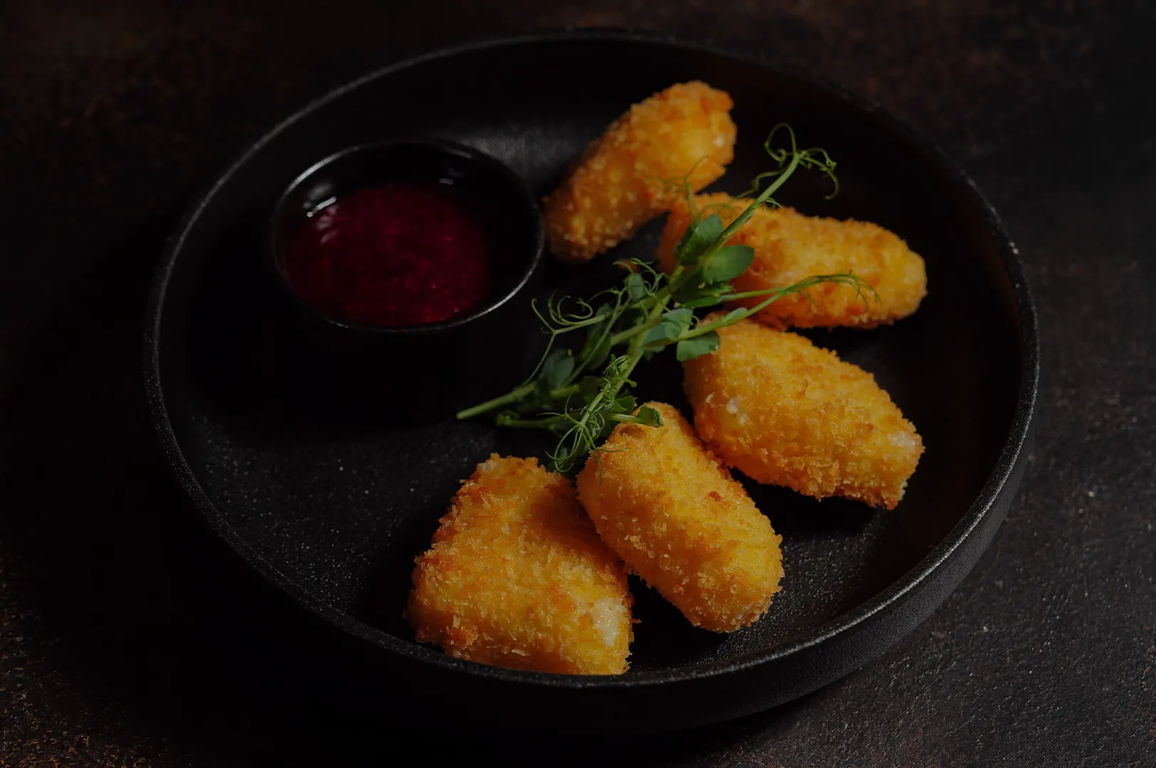 Crispy breaded cheese sticks served with dipping sauce and garnish in a black plate.