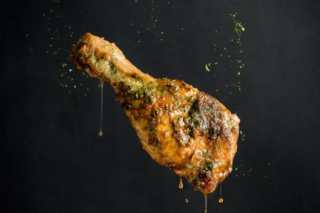 Crispy glazed chicken drumstick with herbs and dripping sauce on a dark background.