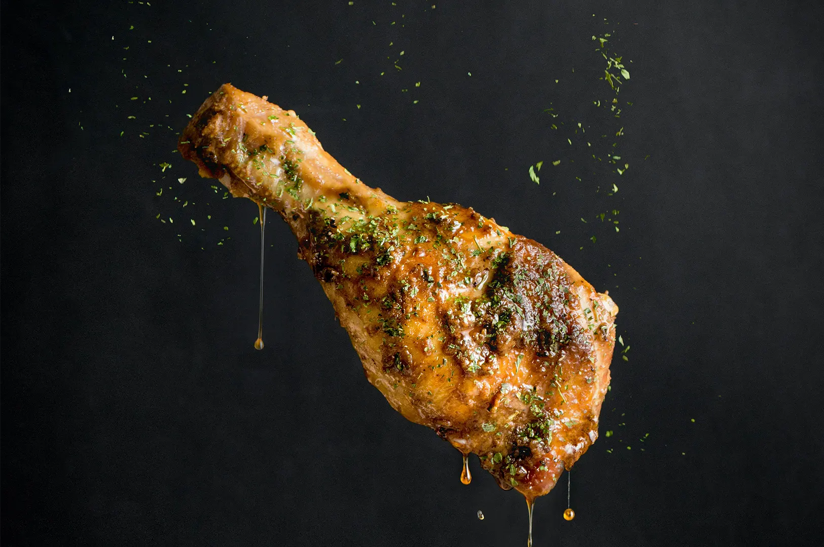 Crispy glazed chicken drumstick with herbs and dripping sauce on a dark background.
