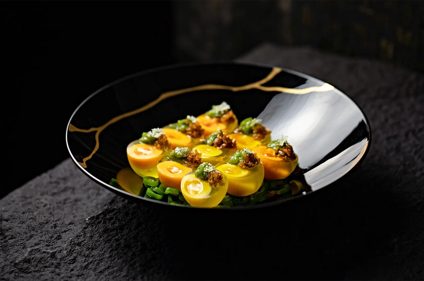 Gourmet deviled eggs with green topping served in a black bowl.