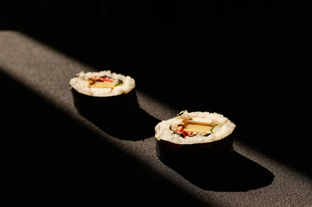 Two pieces of fresh sushi maki rolls served on a black background with dramatic lighting.