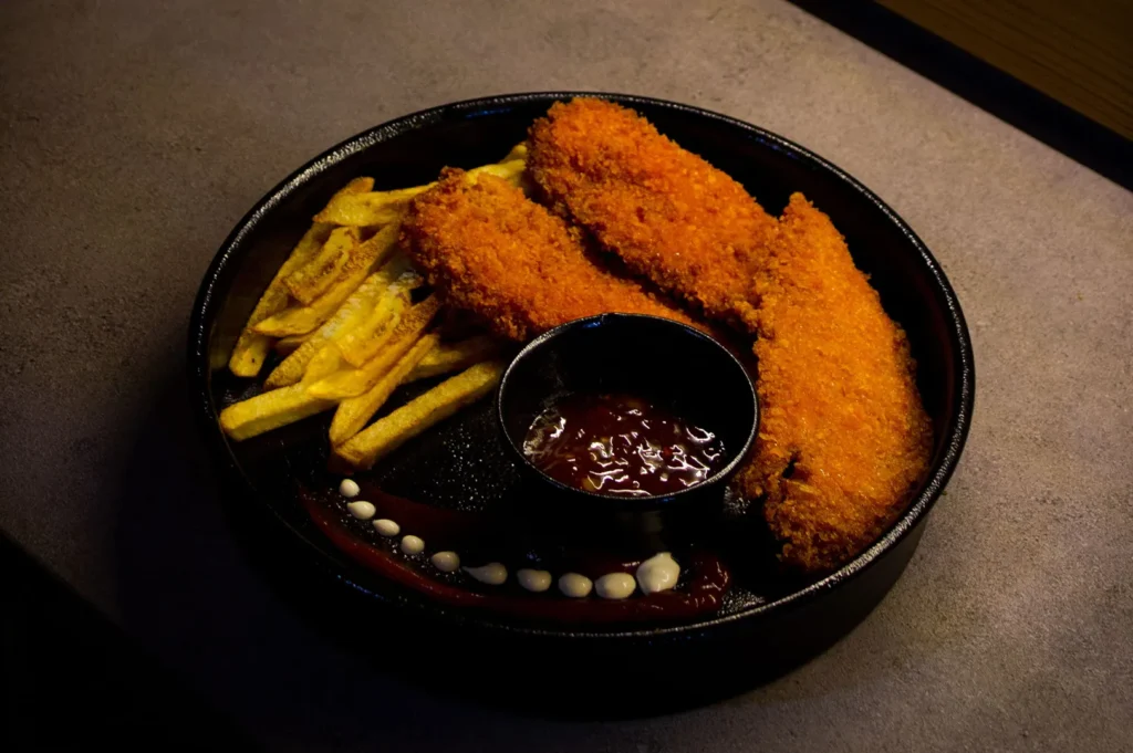 Crispy golden chicken tenders and french fries served with dipping sauce on a dark plate.