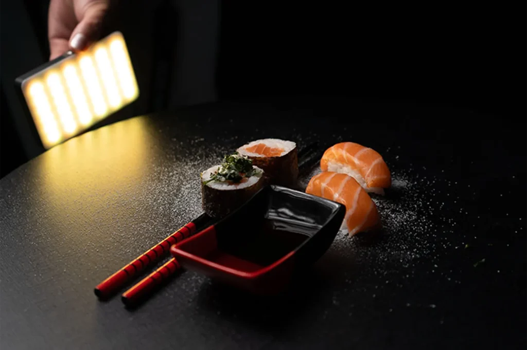 Fresh salmon sushi rolls and nigiri served with soy sauce and chopsticks under studio lighting.