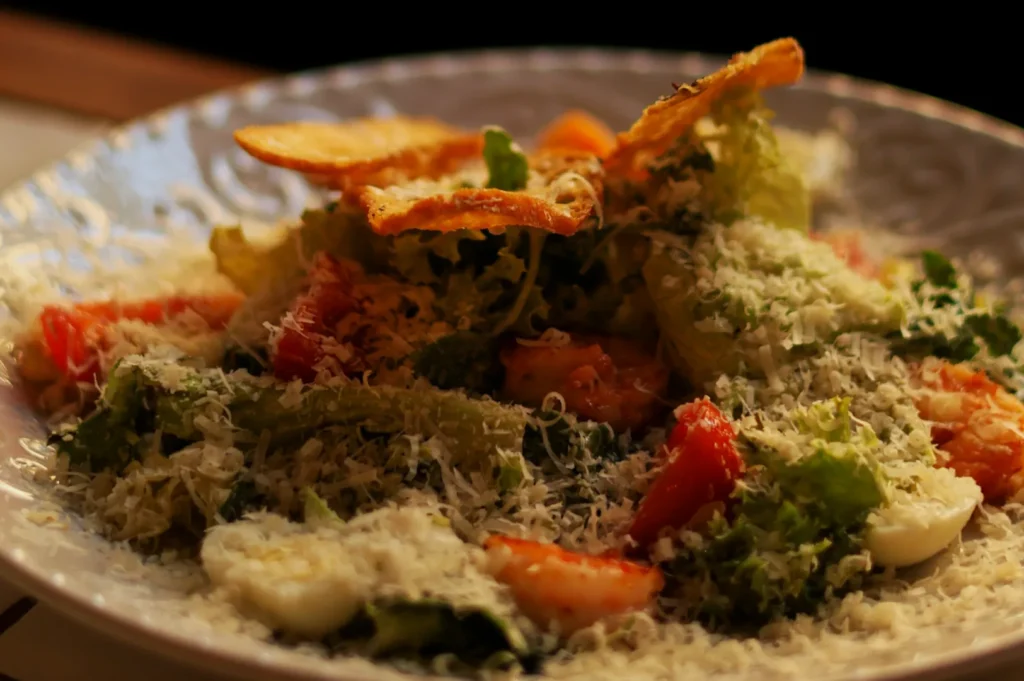 A fresh Caesar salad topped with grated cheese, croutons, and vibrant red tomatoes on a decorative white plate, evoking a savory, appetizing feel.