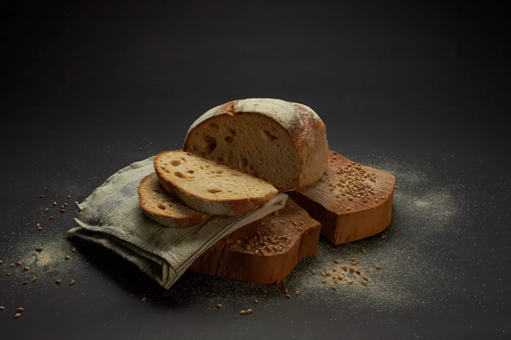 Sliced homemade artisan sourdough bread on a wooden board with flour and grains.