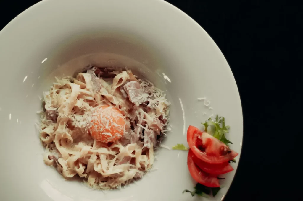 Creamy pasta carbonara with an egg yolk and parmesan cheese served in a white bowl.