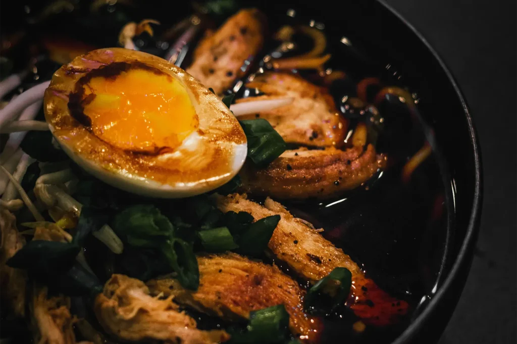 Bowl of ramen noodles topped with a soft-boiled egg, sliced chicken, and green onions.