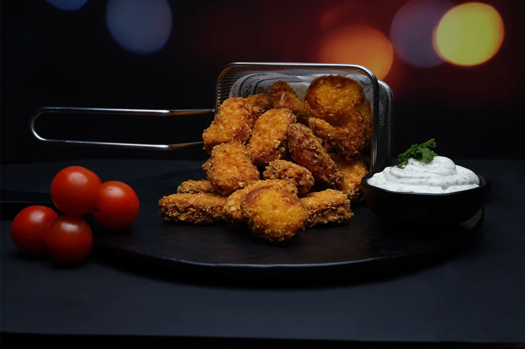 Crispy chicken nuggets served in a metal frying basket with dipping sauce and fresh cherry tomatoes.