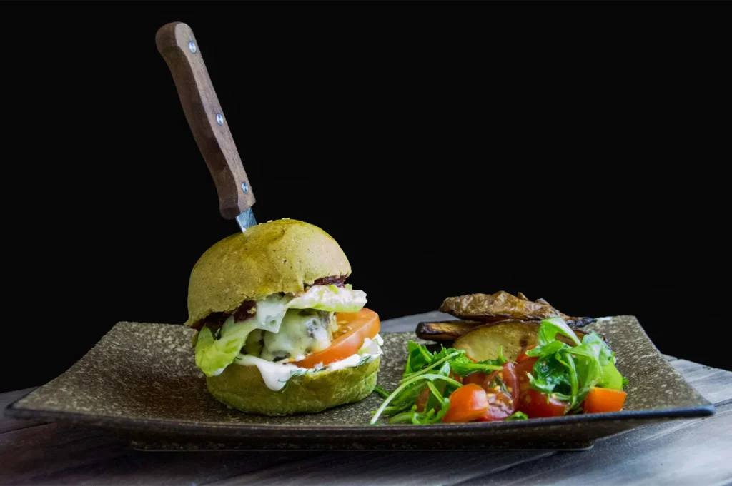 White balance photography of a gourmet green burger with a knife, potato wedges, and fresh salad.