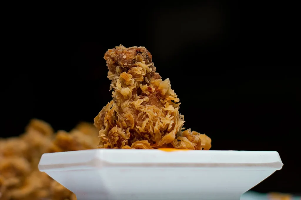 Crispy golden-brown fried chicken wing served on a white plate against a dark background.