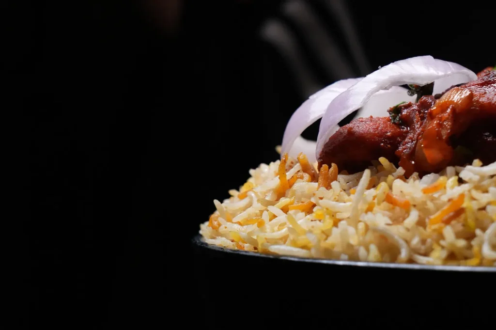 Delicious chicken biryani with spiced rice and onion garnish on a dark background.