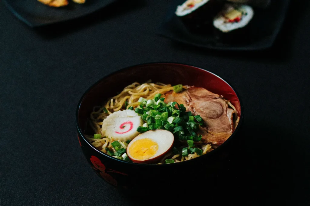 A bowl of Japanese ramen noodles topped with chashu pork, soft-boiled egg, and green onions.