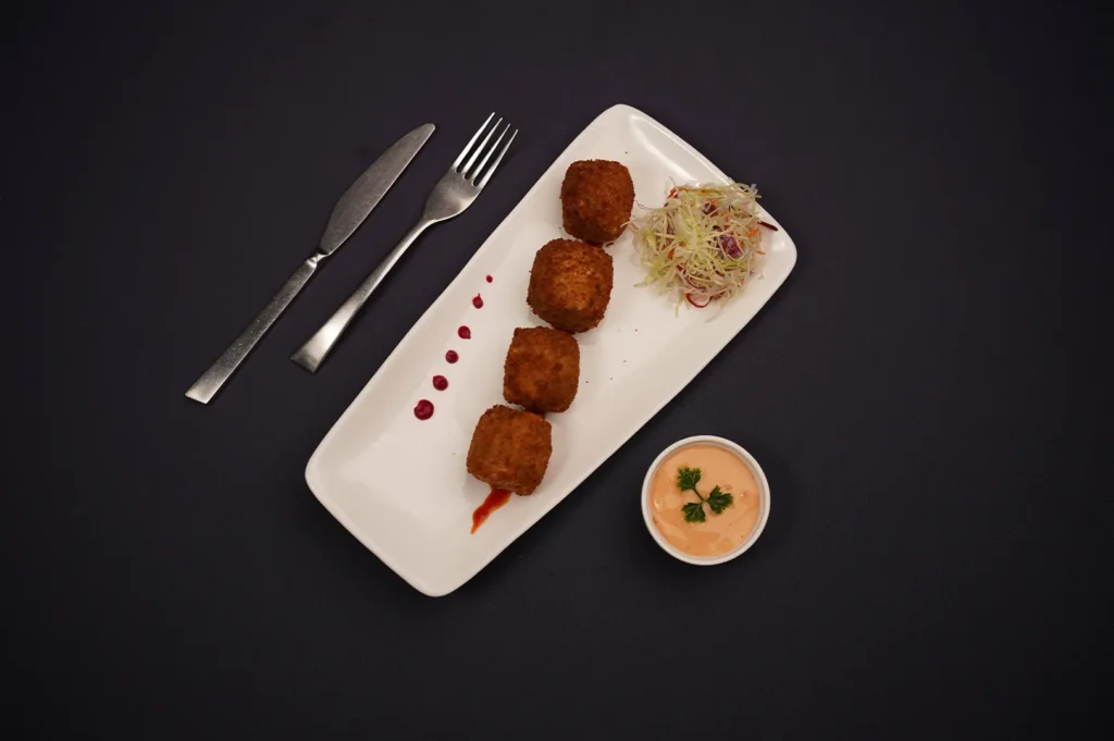 Crispy fried croquettes served with a side salad and dipping sauce on a white plate.
