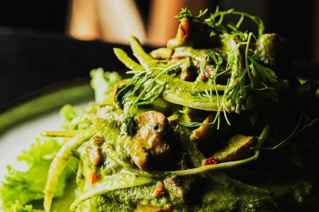 Close-up of a vibrant green salad with mixed greens, snap peas, mushrooms, and herbs. The dish looks fresh and appetizing against a dark background.