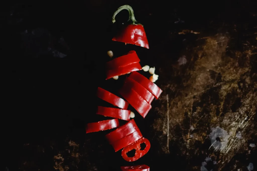 Moody black food photography of freshly sliced red chili pepper showing crisp edge texture and natural movement on a dark background.
