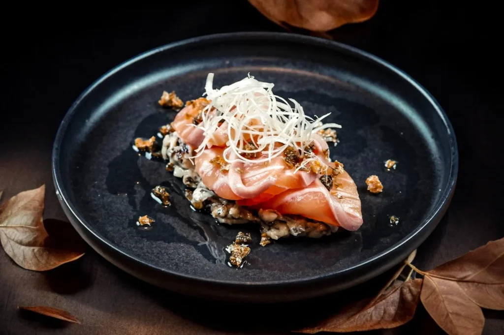 Gourmet salmon tartare with white garnish on a dark plate, food photography.