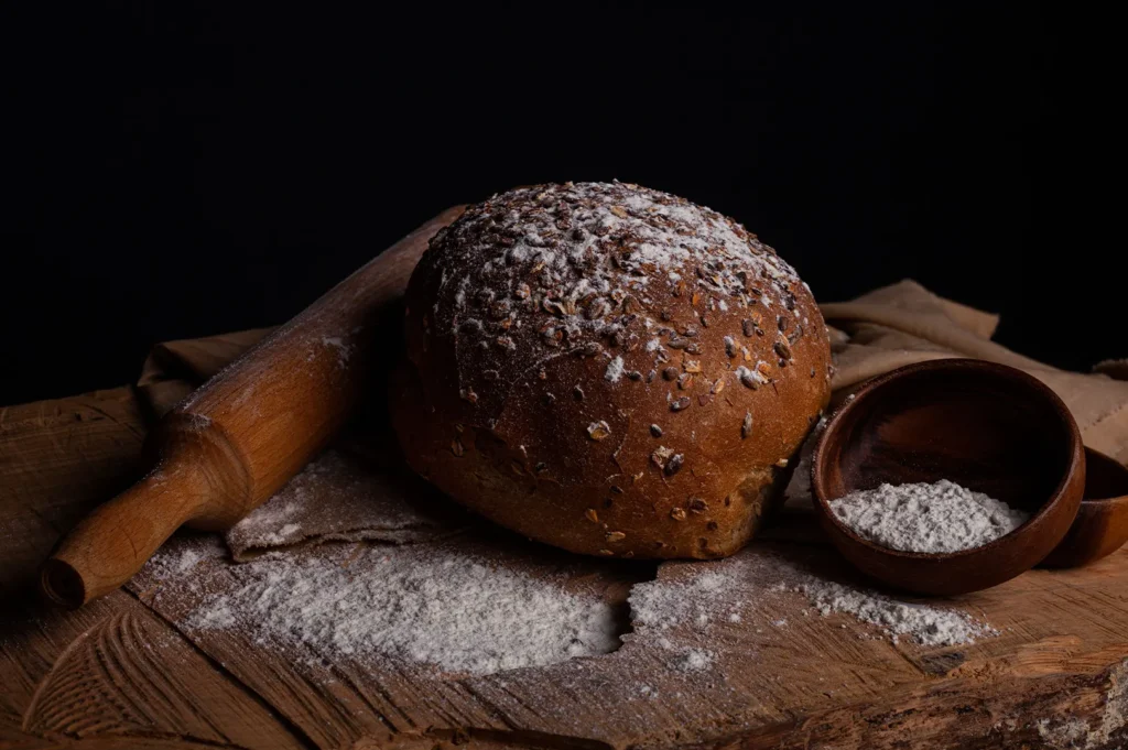 Freshly baked seeded bread loaf with a wooden rolling pin and flour on a board.