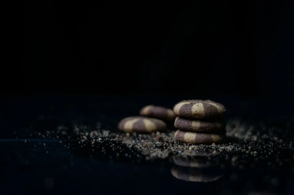 Stack of chocolate and vanilla striped cookies on a black background with crumbs.