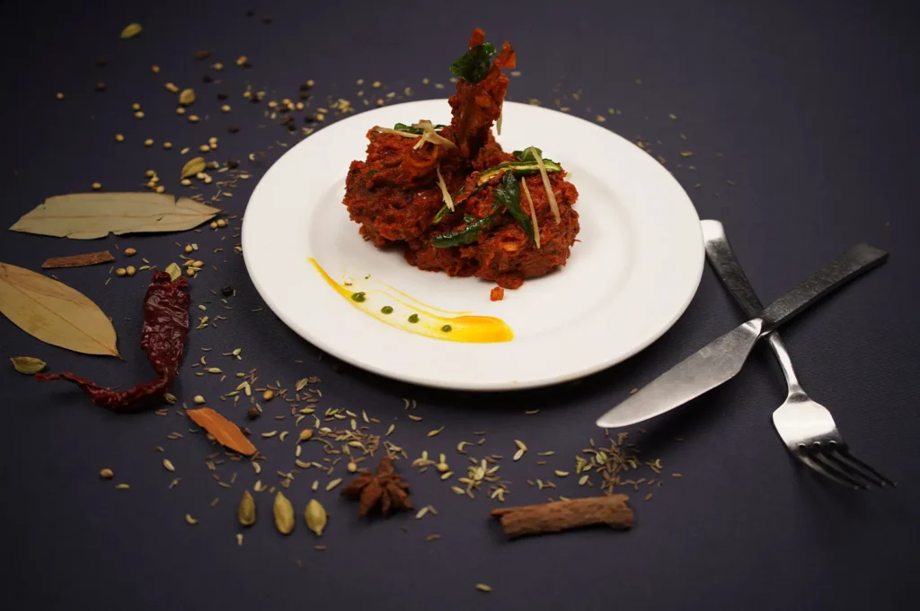 Spicy Indian mutton or chicken dish served on a white plate with whole spices and cutlery.