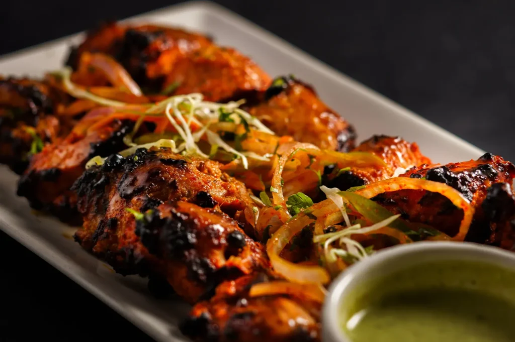 Delicious homemade chicken tikka served with sliced onions and green mint chutney on a white plate.