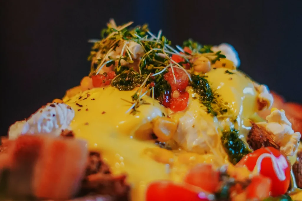 Close-up of a colorful dish with creamy yellow sauce, fresh greens, diced tomatoes, and herbs, evoking a fresh and indulgent culinary experience.