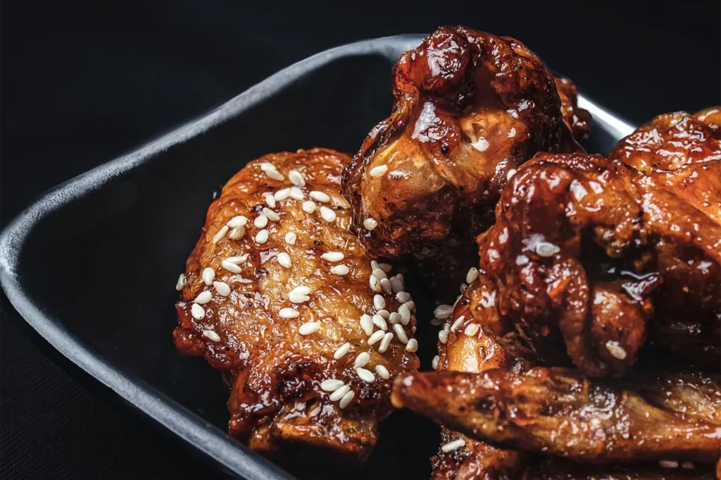 Crispy glazed chicken wings sprinkled with white sesame seeds in a black plate.