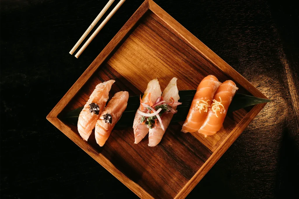 Food photography of gourmet nigiri sushi platter served on a wooden tray with chopsticks.