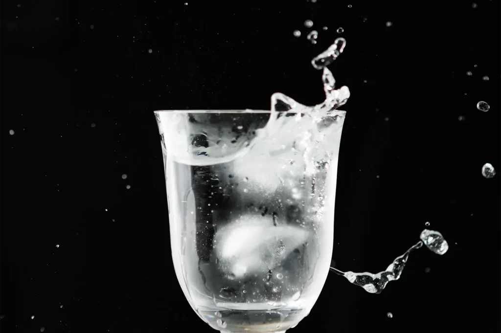 Water splashing out of a glass with ice cubes against a black background.