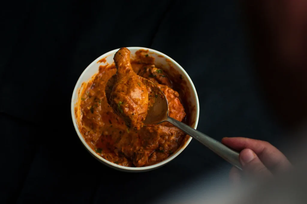 Close-up of a chicken dish with rich clinging sauce in a dark background setting.