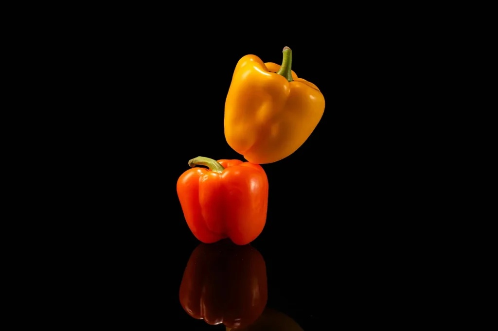 Fresh orange and yellow bell peppers on a black reflective background.