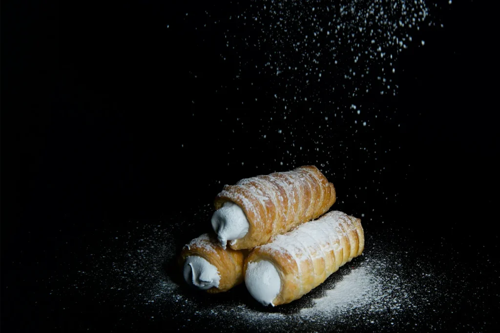Three cream horns dusted with powdered sugar on a black background.