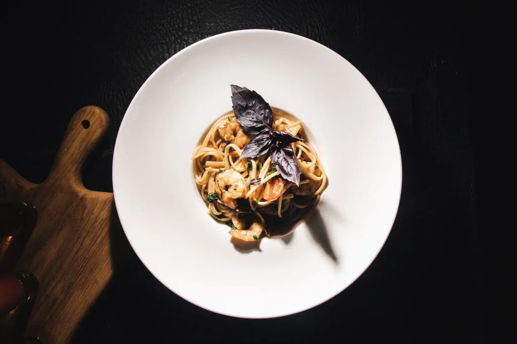 Gourmet shrimp pasta served in a white bowl and garnished with fresh purple basil leaves