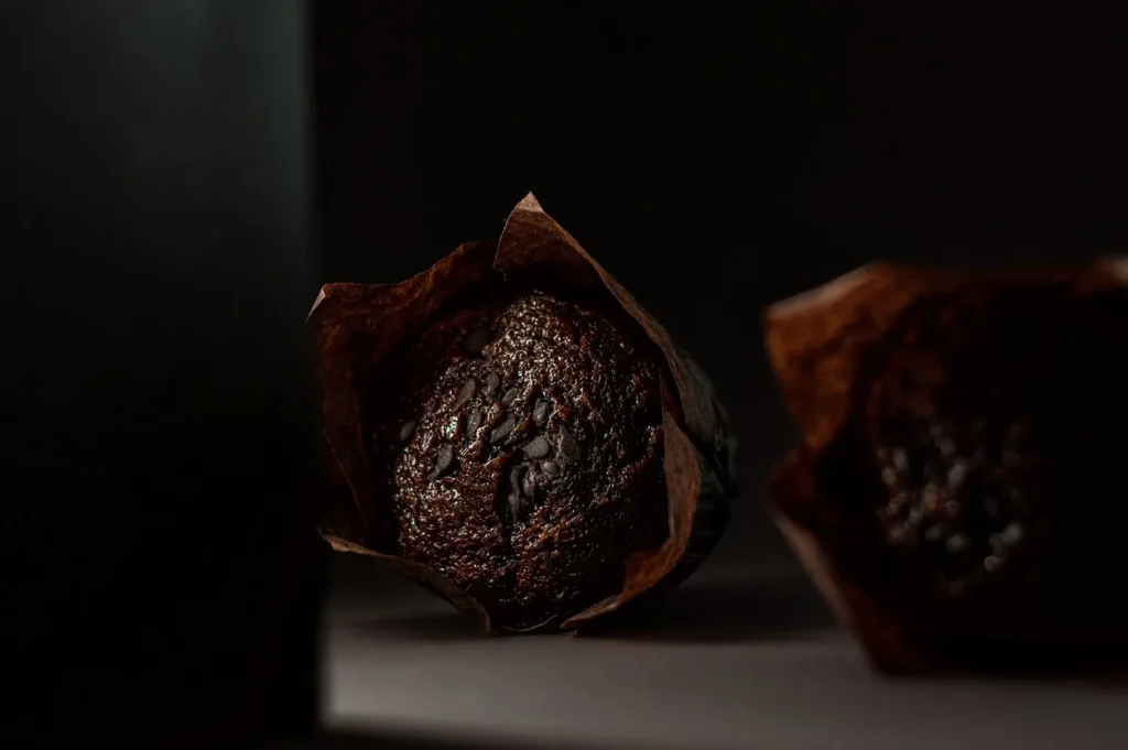Freshly baked chocolate muffin with chocolate chips in a paper liner on a dark background.