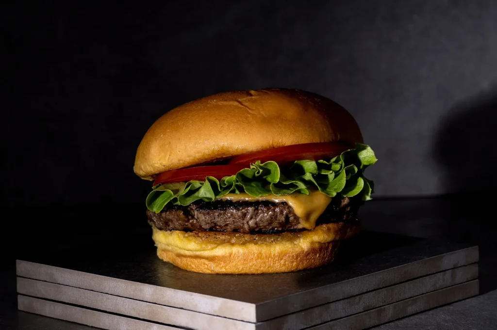 Juicy cheeseburger with fresh lettuce, tomato, and a grilled beef patty on a dark background.