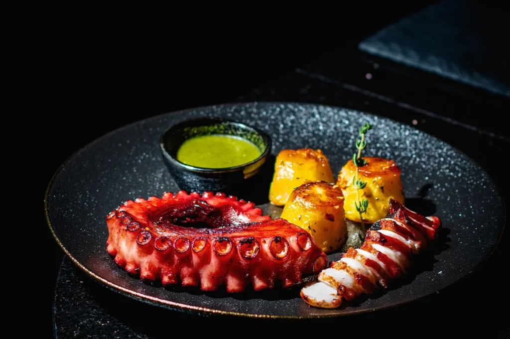 Moody food photography of grilled octopus on a black plate with side lighting.