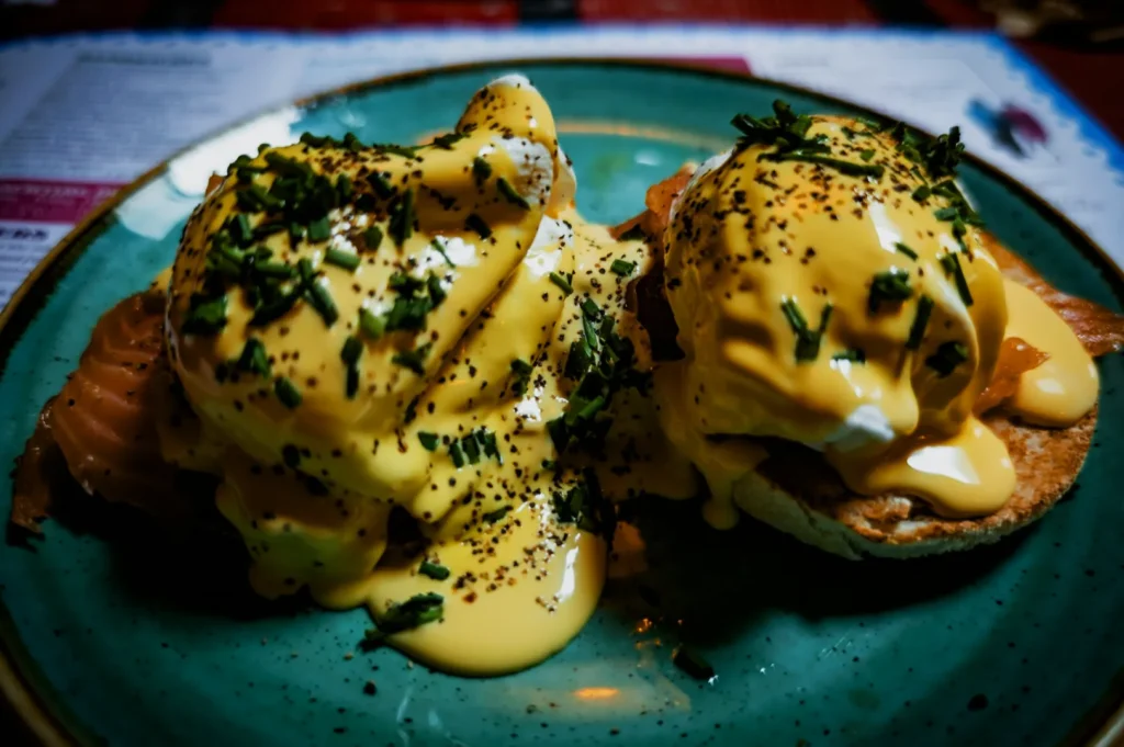 Eggs Benedict on a green plate, topped with creamy hollandaise sauce, sprinkled with chives and pepper, evokes a rich and savory brunch vibe.