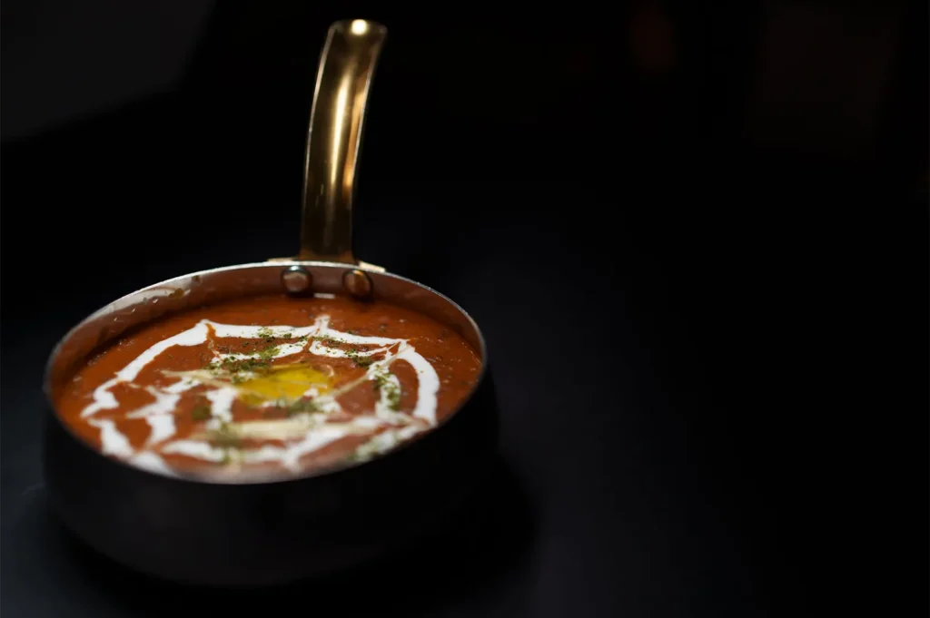 A rich, creamy bowl of Dal Makhani garnished with fresh cream and butter served in a traditional metal pot.