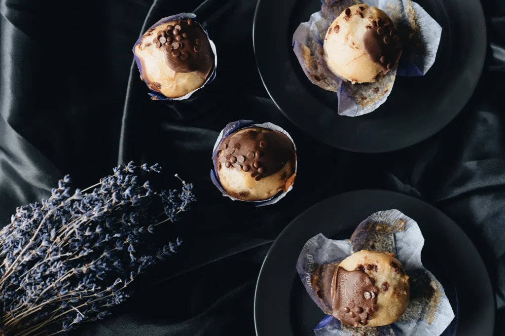 Freshly baked chocolate-topped muffins on dark plates with a bunch of dried lavender.