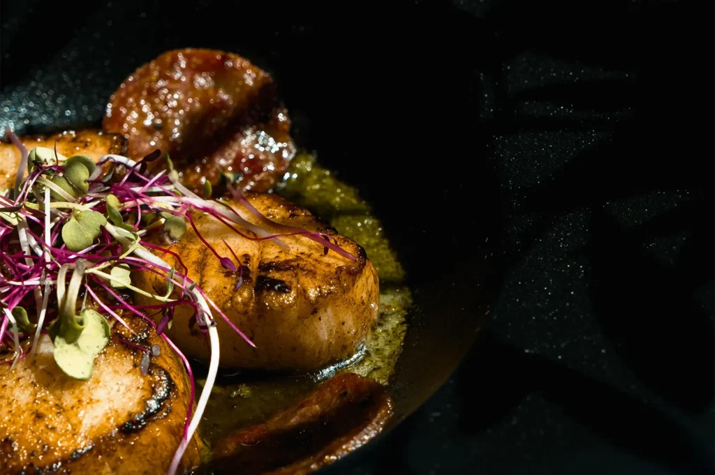 Food photography of seared scallops using a flag to block glare and create deep shadows for dramatic lighting.