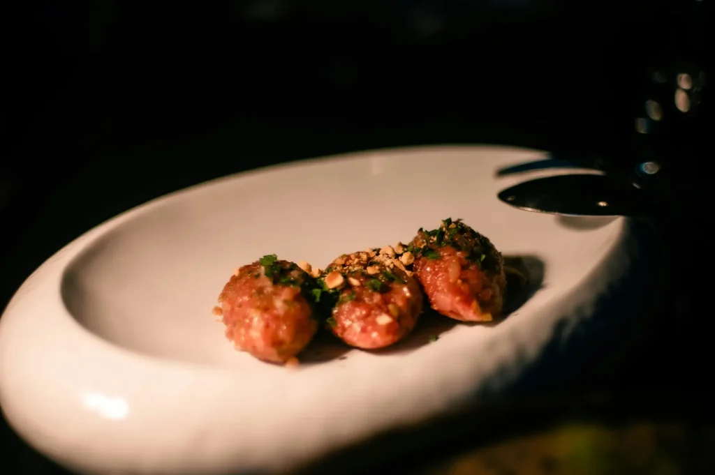 Gourmet steak tartare bites garnished with herbs and nuts served on a white oval plate.