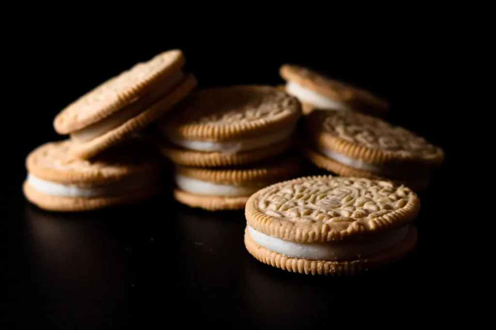Golden sandwich cookies with white cream filling stacked on a black background.