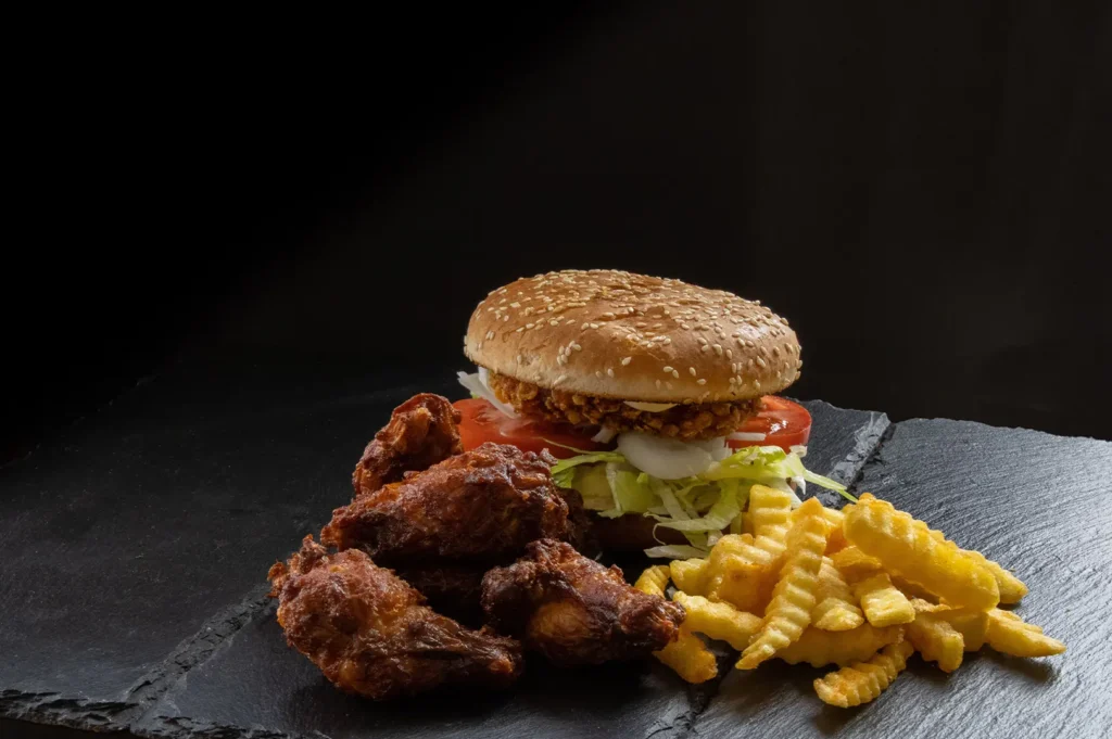 Crispy chicken burger with fried chicken wings and french fries on a dark slate board.