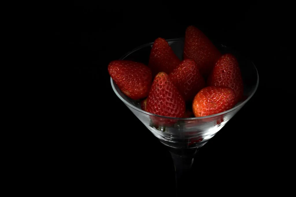 Fresh red strawberries in a glass bowl against a black background.