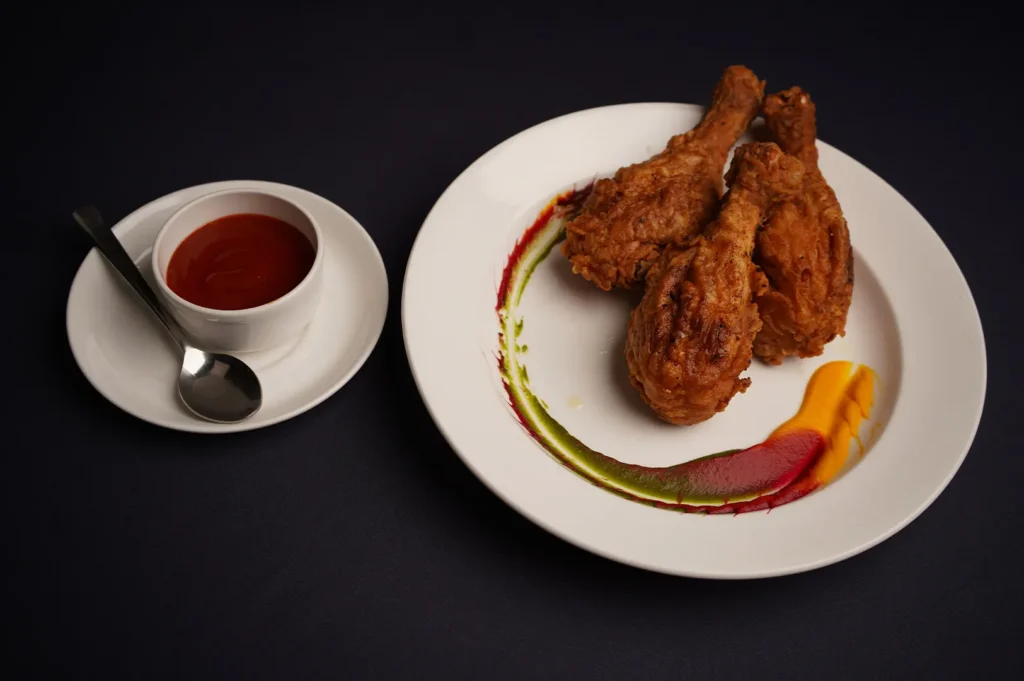 Crispy fried chicken drumsticks served on a white plate with dipping sauce and colorful garnish.