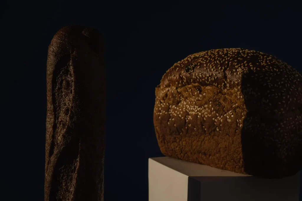 Freshly baked artisanal whole-grain bread and sesame seed loaf on display against a dark background.