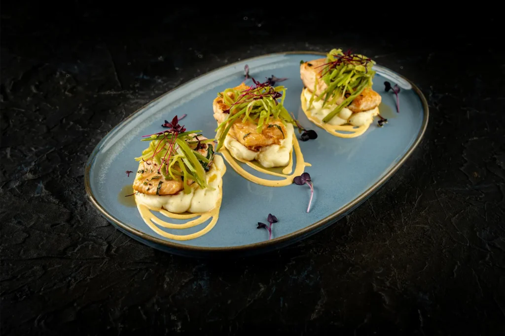 Pan-seared fish fillets with mashed potatoes and green garnish on a blue plate.